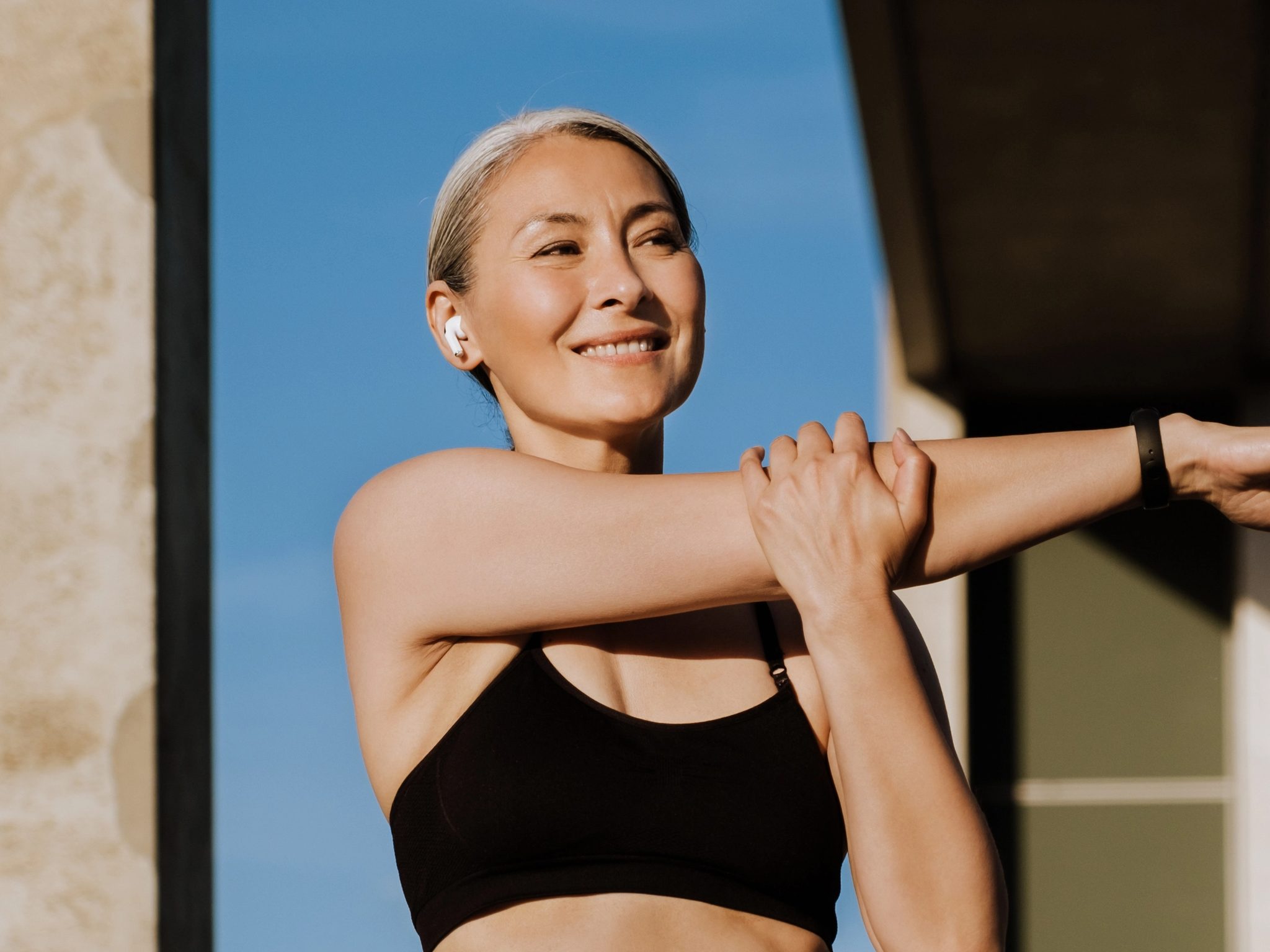 Woman in athletic wear stretching arm in front of a modern building
