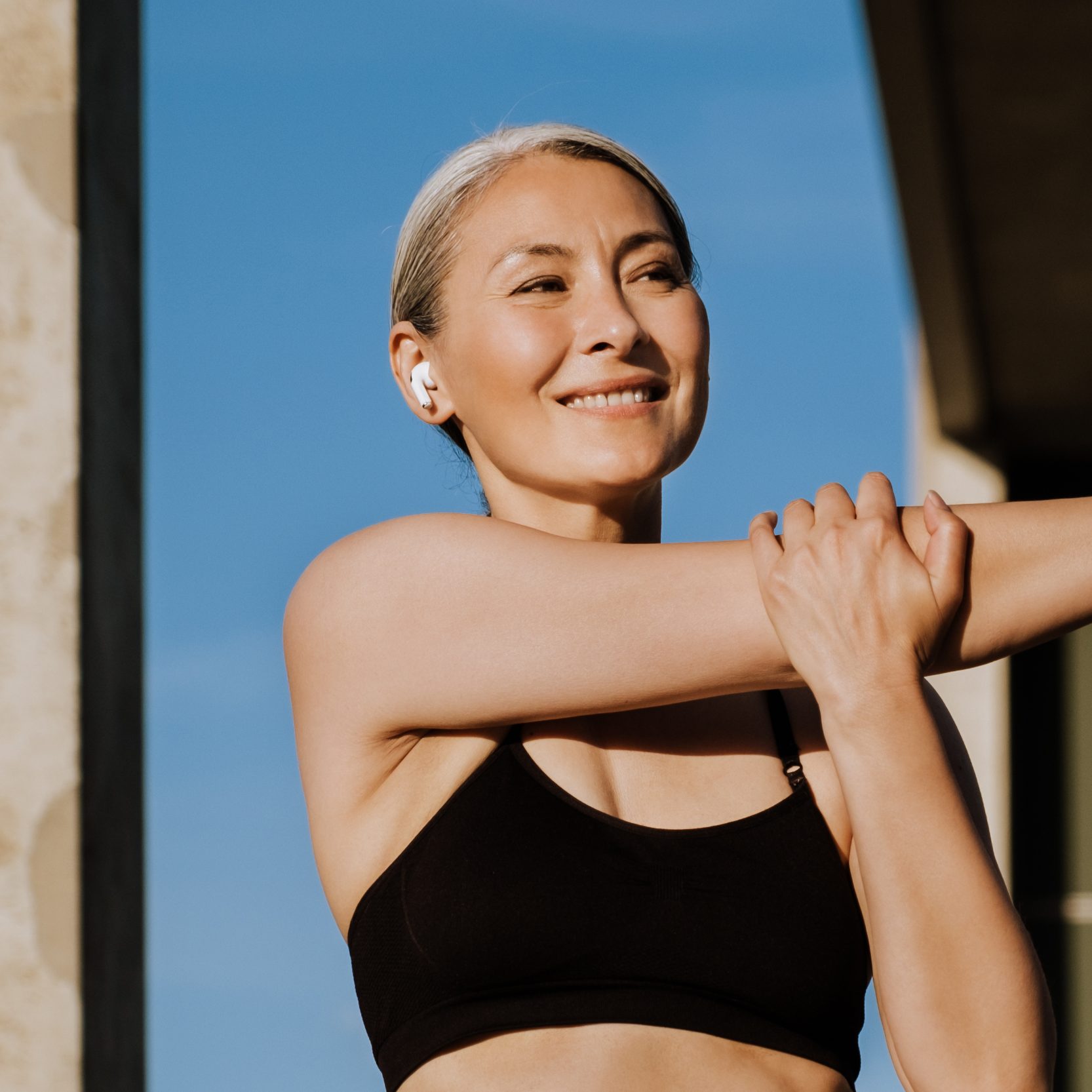 Woman in athletic wear stretching arm in front of a modern building
