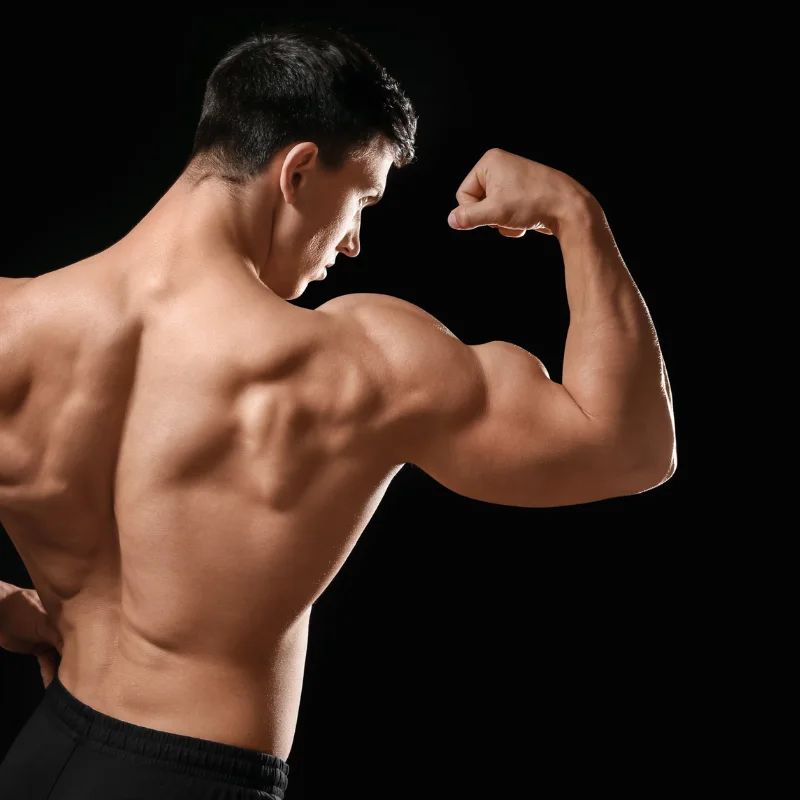 Muscular shirtless man flexing his bicep, seen from behind against a black background