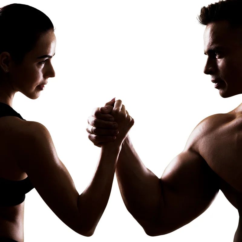 Silhouettes of a fit man and woman arm wrestling against a white background
