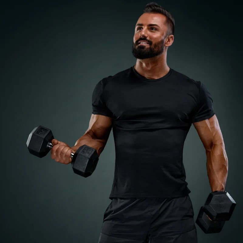 Athletic bearded man holding dumbbells against a dark studio background