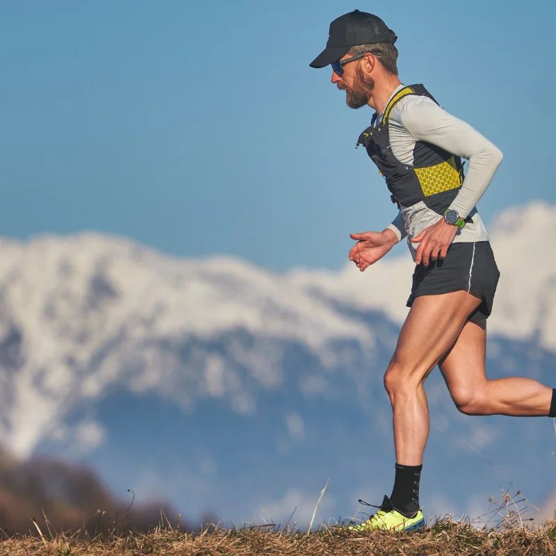 Man trail running across a grassy ridge with snow-capped mountains in the background