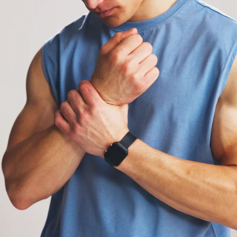 Man in a blue tank top gripping his sore wrist below a smartwatch